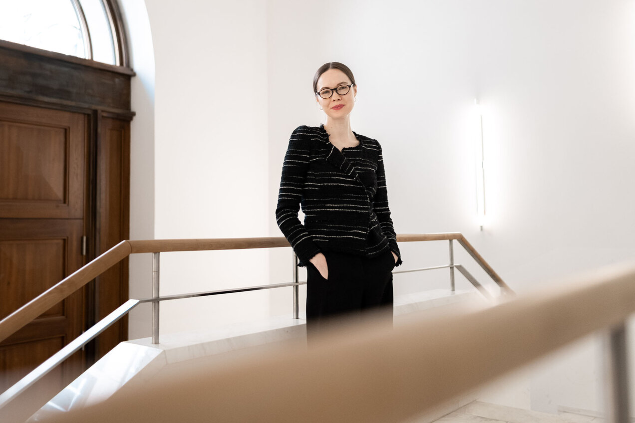portrait of Elena Beregow leaning against a banister of a stairwell, a large wooden door in the background