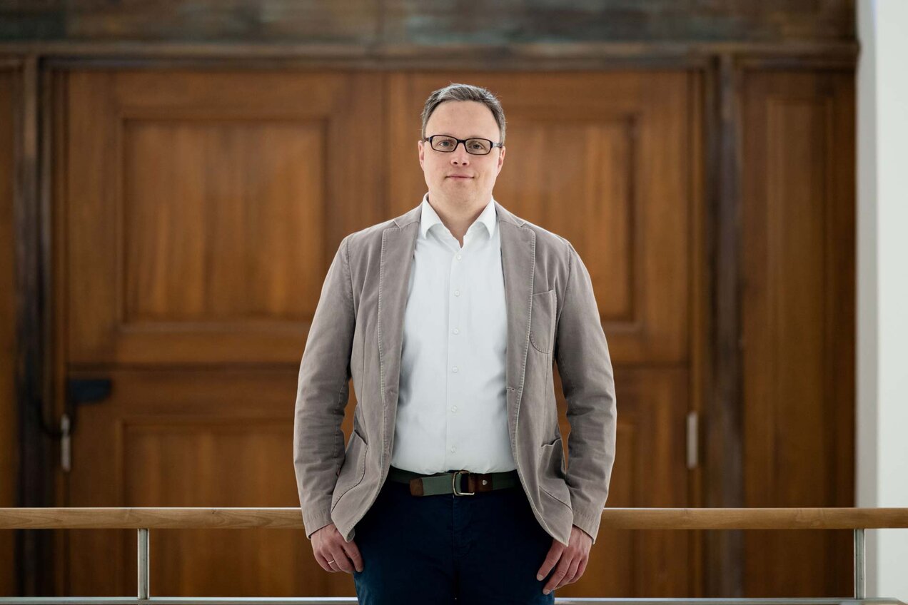 Matthias Kranke leaning against a bannister, a wooden door behind him