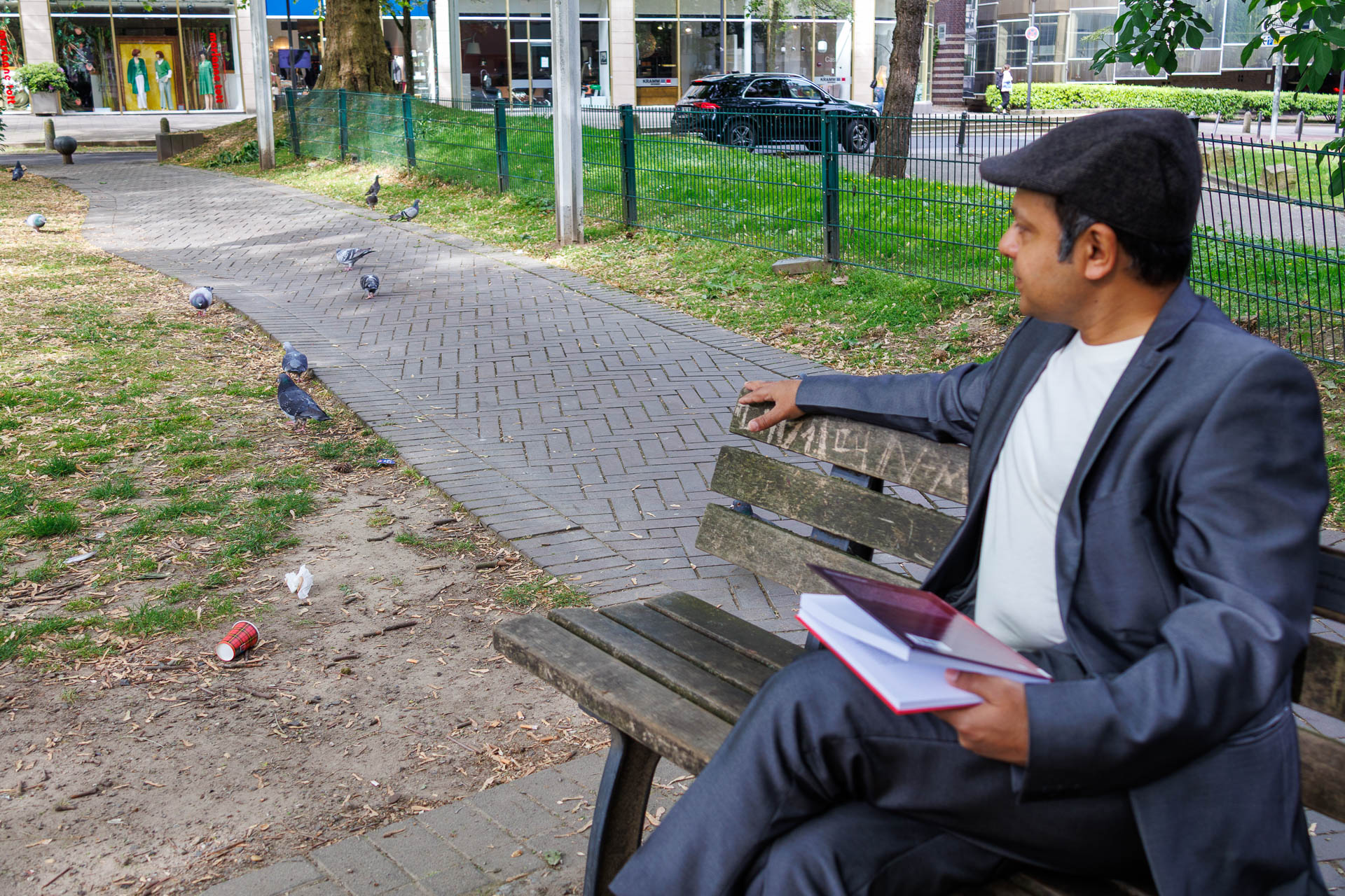 Imran Sabir sitting on a wooden bench, looking at several pidgeons next to the bench