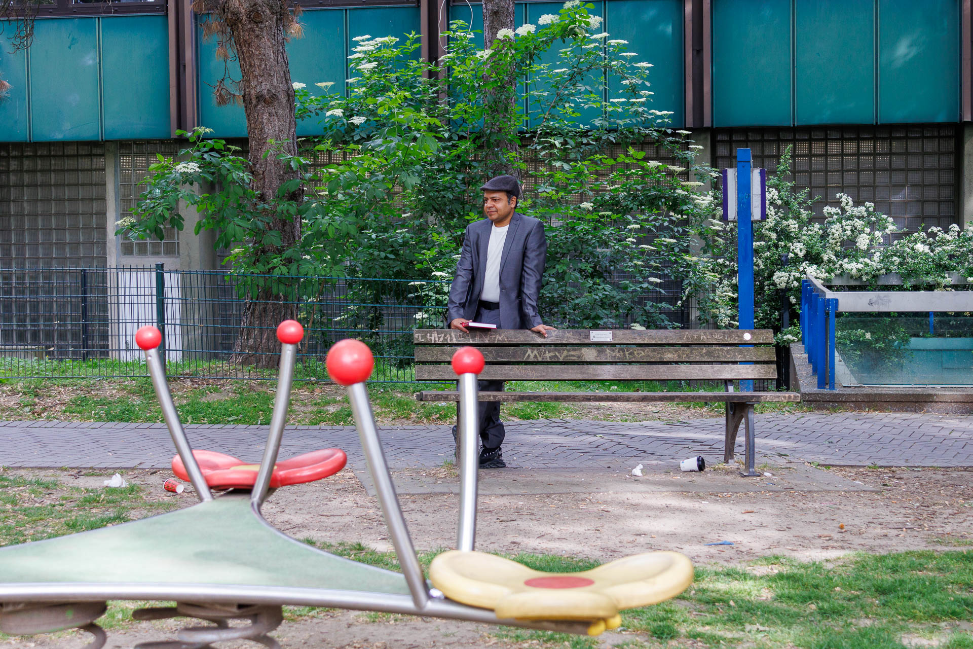 Close-up of a play structure on a playground. Imran Sabir leaning on a bench in the background.