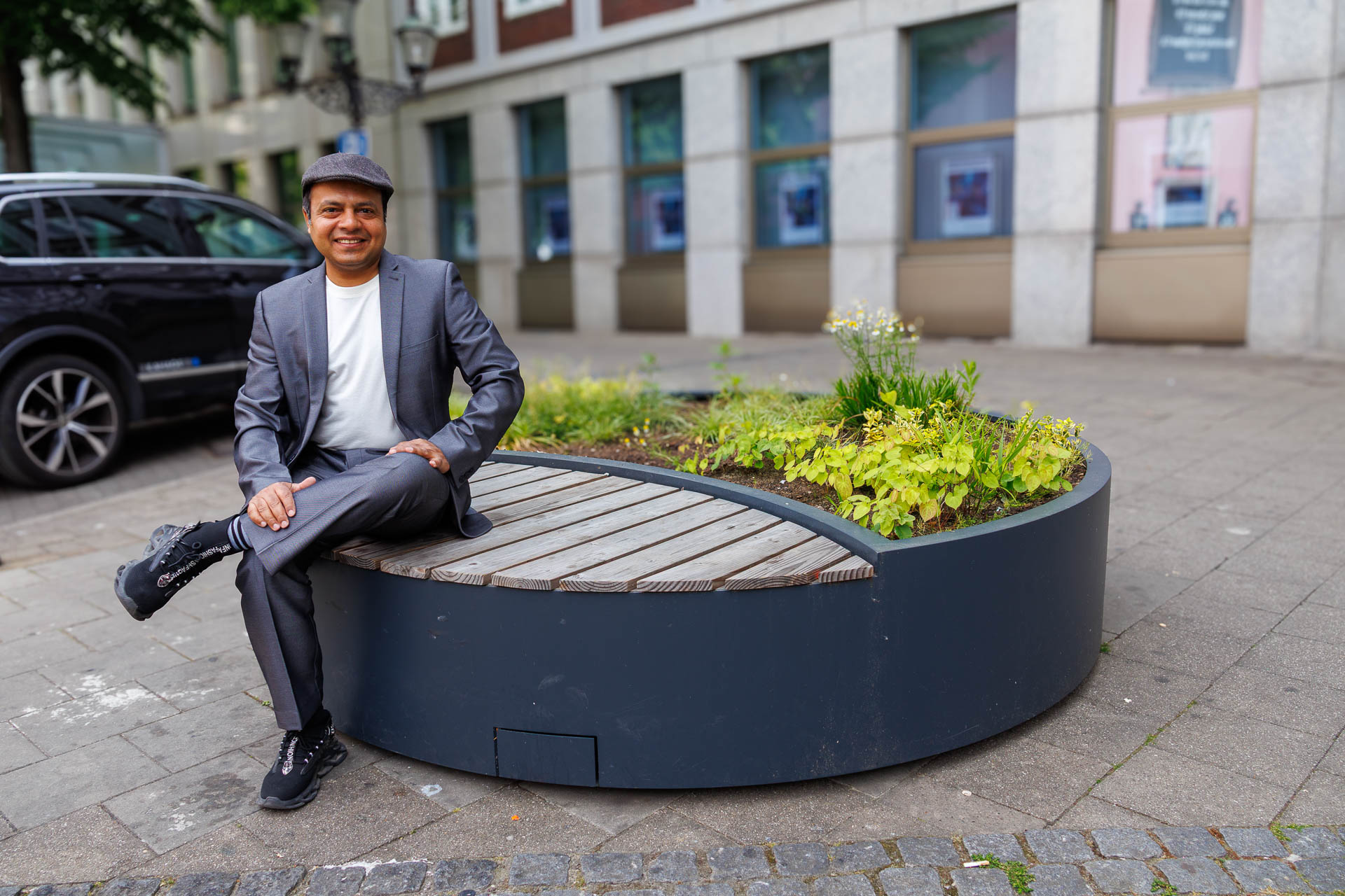 Imran Sabir smiling at the camera sitting on a bench that is connected to a flowerbed.