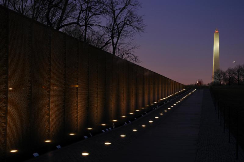 a picture of the Vietnam Veterans Memorial Wall, a wall with names engraved and a column in the background, at twilight
