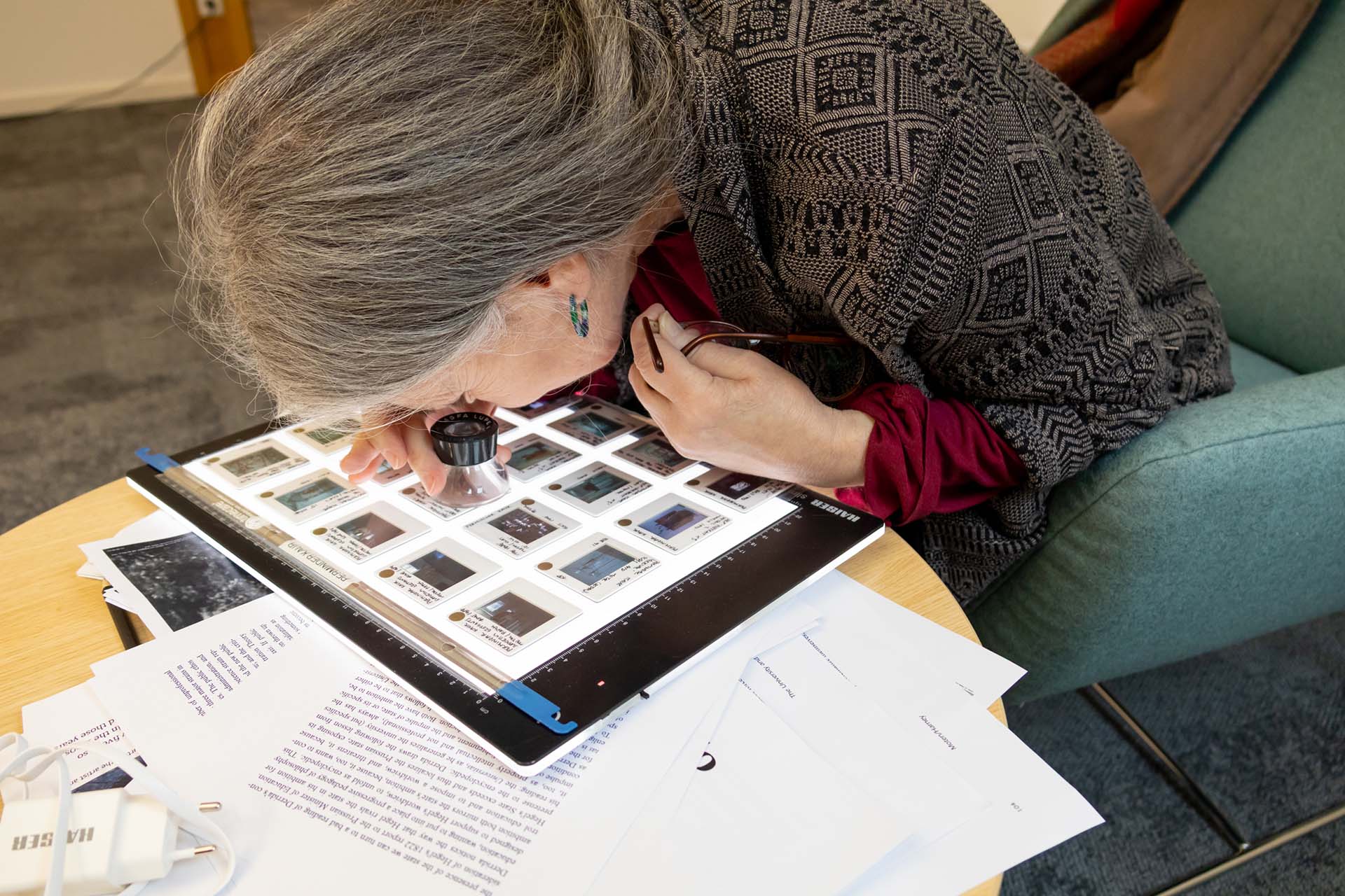 Althea Greenan looking at the small slides of photographs through a magnifying glass