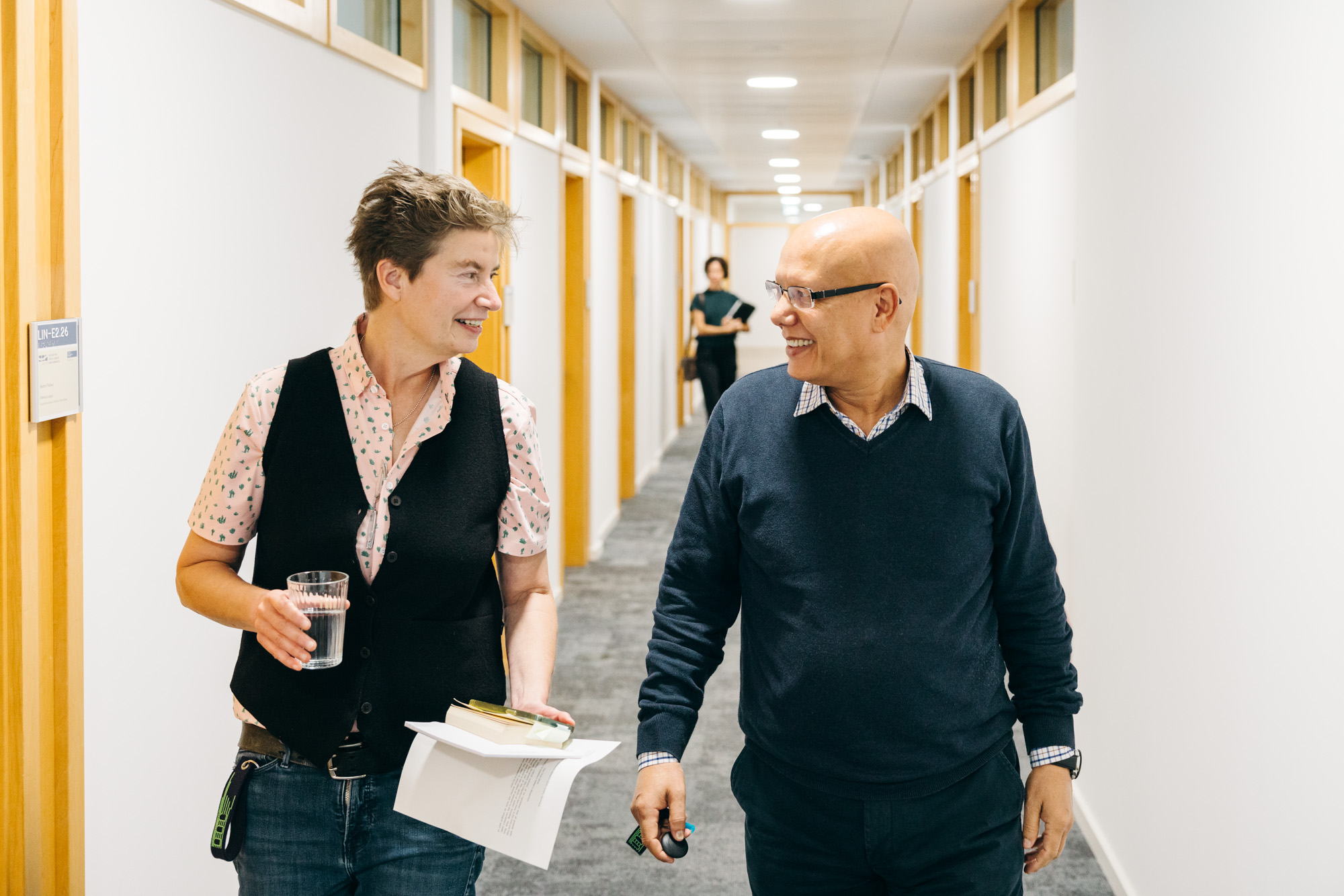 two persons walking down a hallway beside each other, looking at each other
