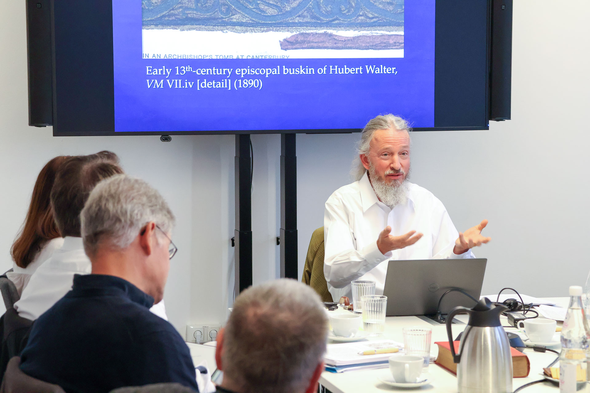photo from the workshop 'Editing Journal Literature', participants sitting around a table, a speaker presenting, a screen with slides in the back