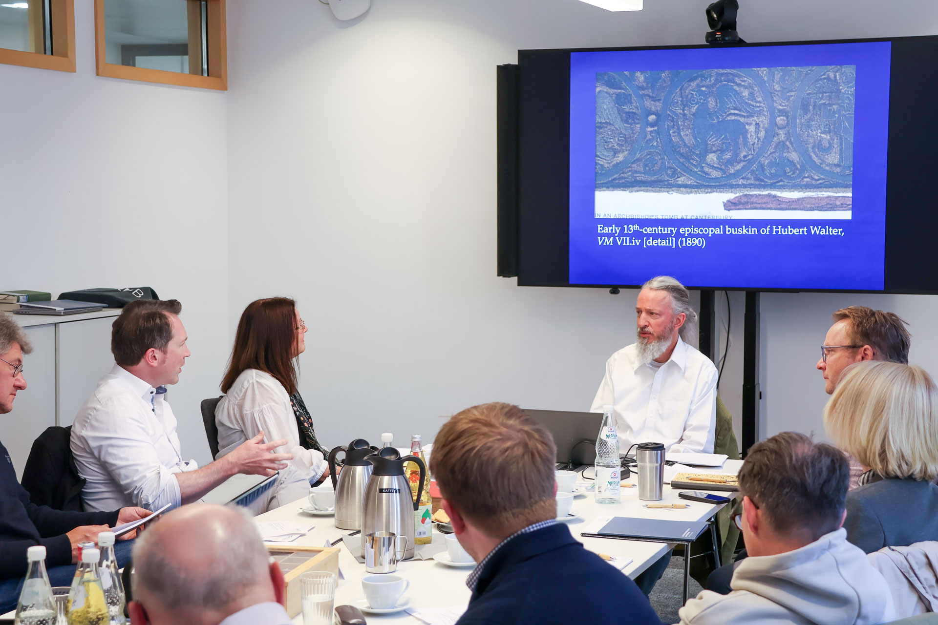 photo from the workshop 'Editing Journal Literature', participants sitting around a table, a speaker presenting, a screen with slides in the back