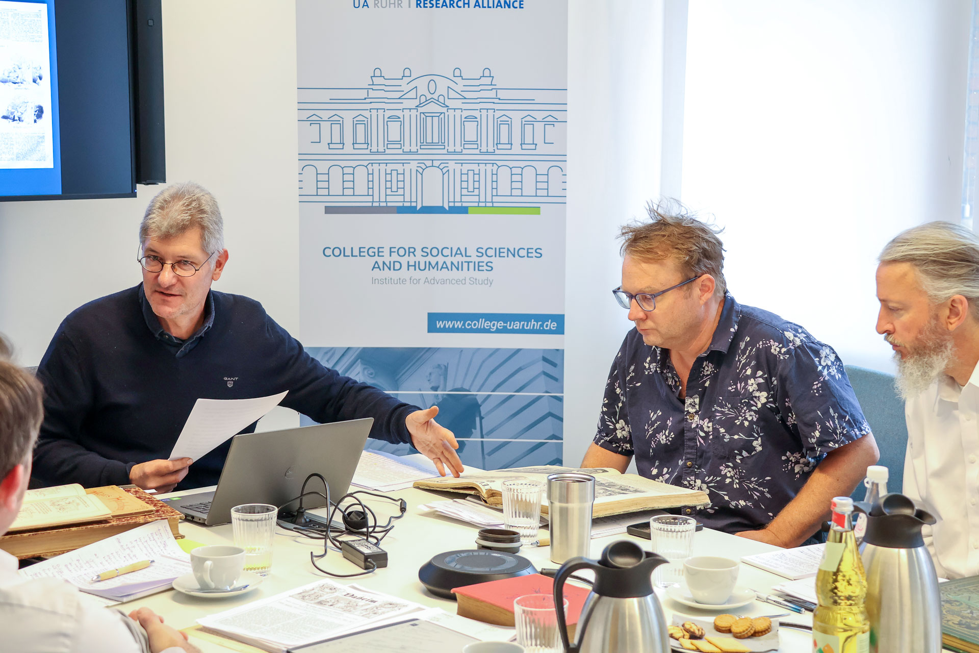 photo from the workshop 'Editing Journal Literature', participants sitting around a table, a speaker presenting, a screen with slides in the back
