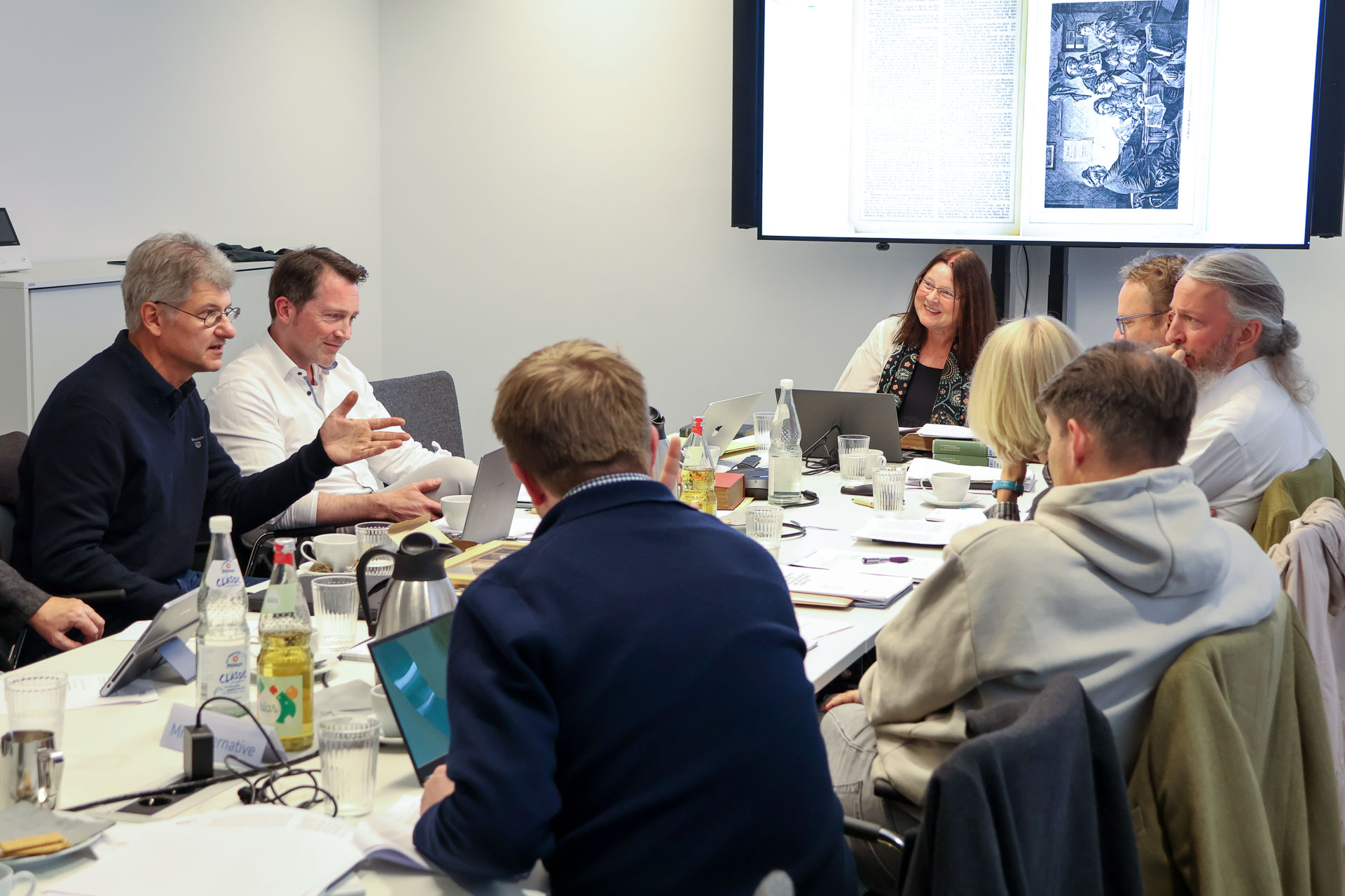 photo from the workshop 'Editing Journal Literature', participants sitting around a table, a speaker presenting, a screen with slides in the back