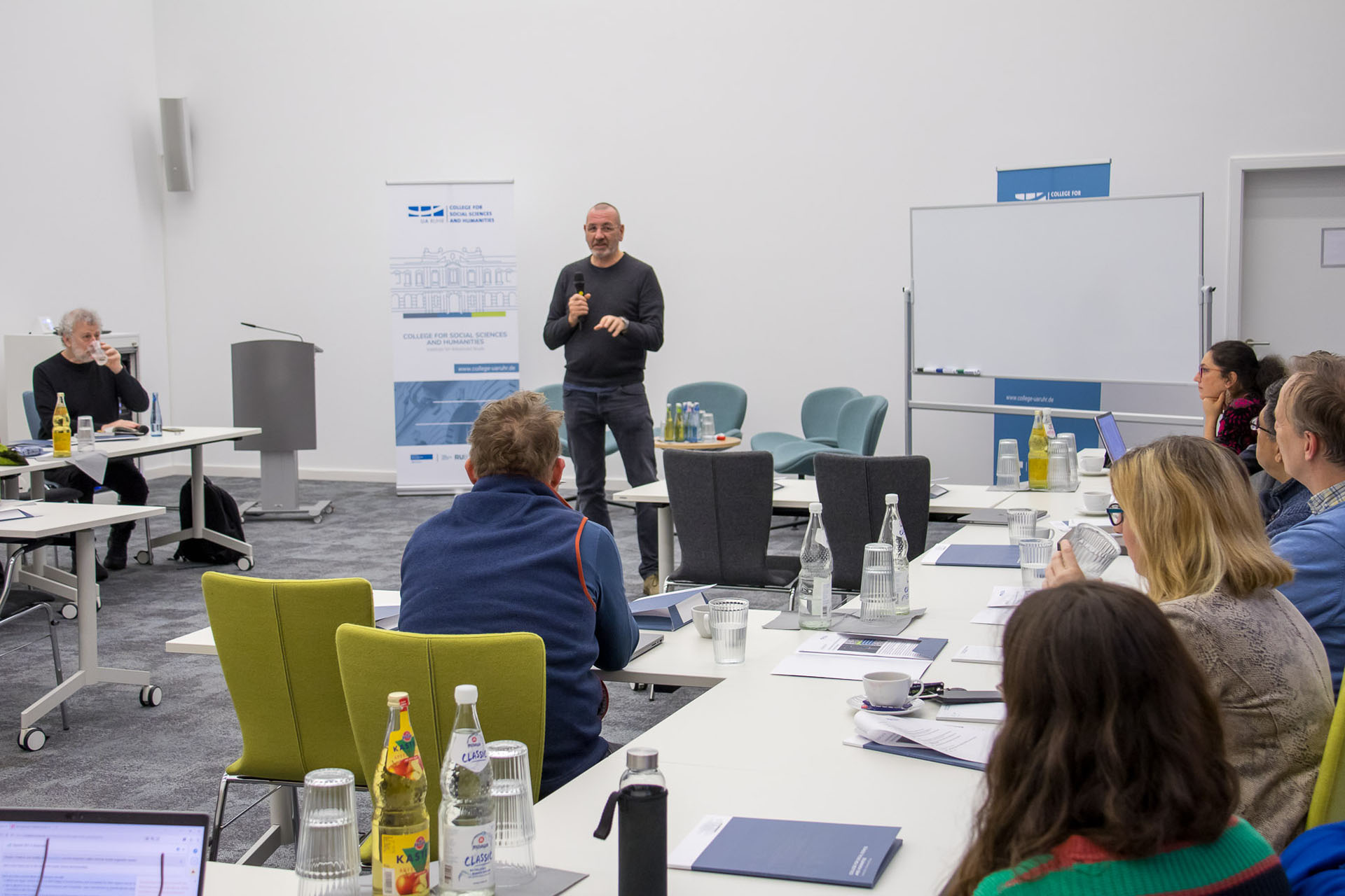 photo from the workshop, Prof. Gudehus standing and presenting, participants sitting at tables