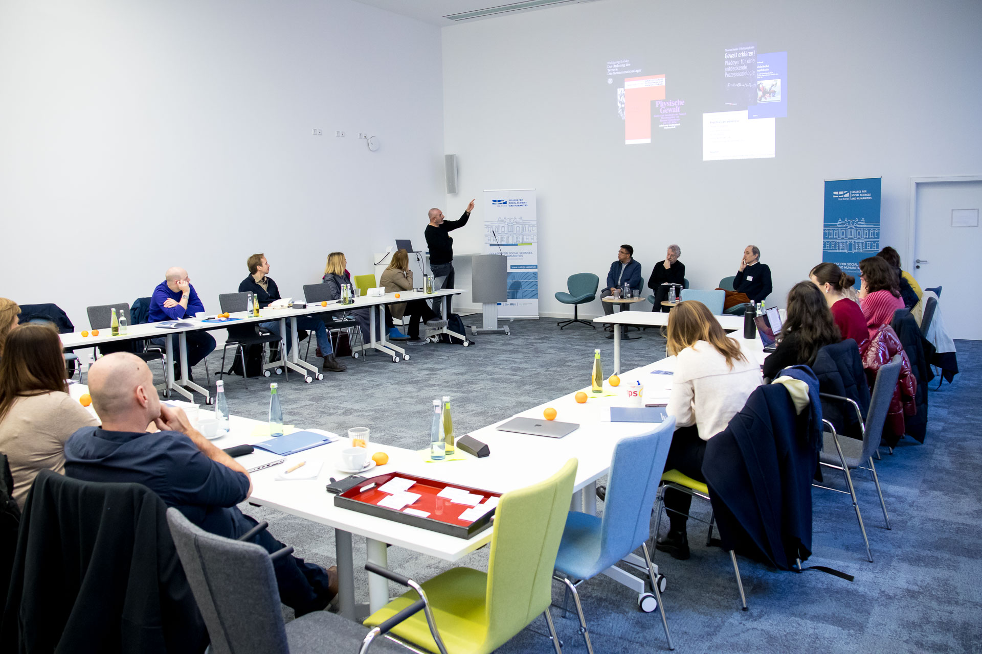 photo from the workshop 'Perpetrator Memory in Spanish culture', participants sitting at a table, a speaker presenting, a screen with slides in the back