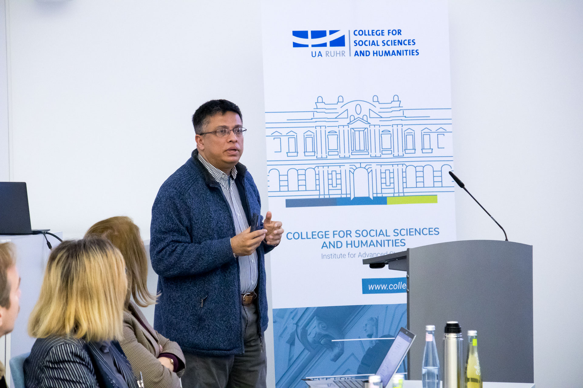 photo from the workshop 'Perpetrator Memory in Spanish culture', participants sitting at a table, a speaker presenting, a screen with slides in the back