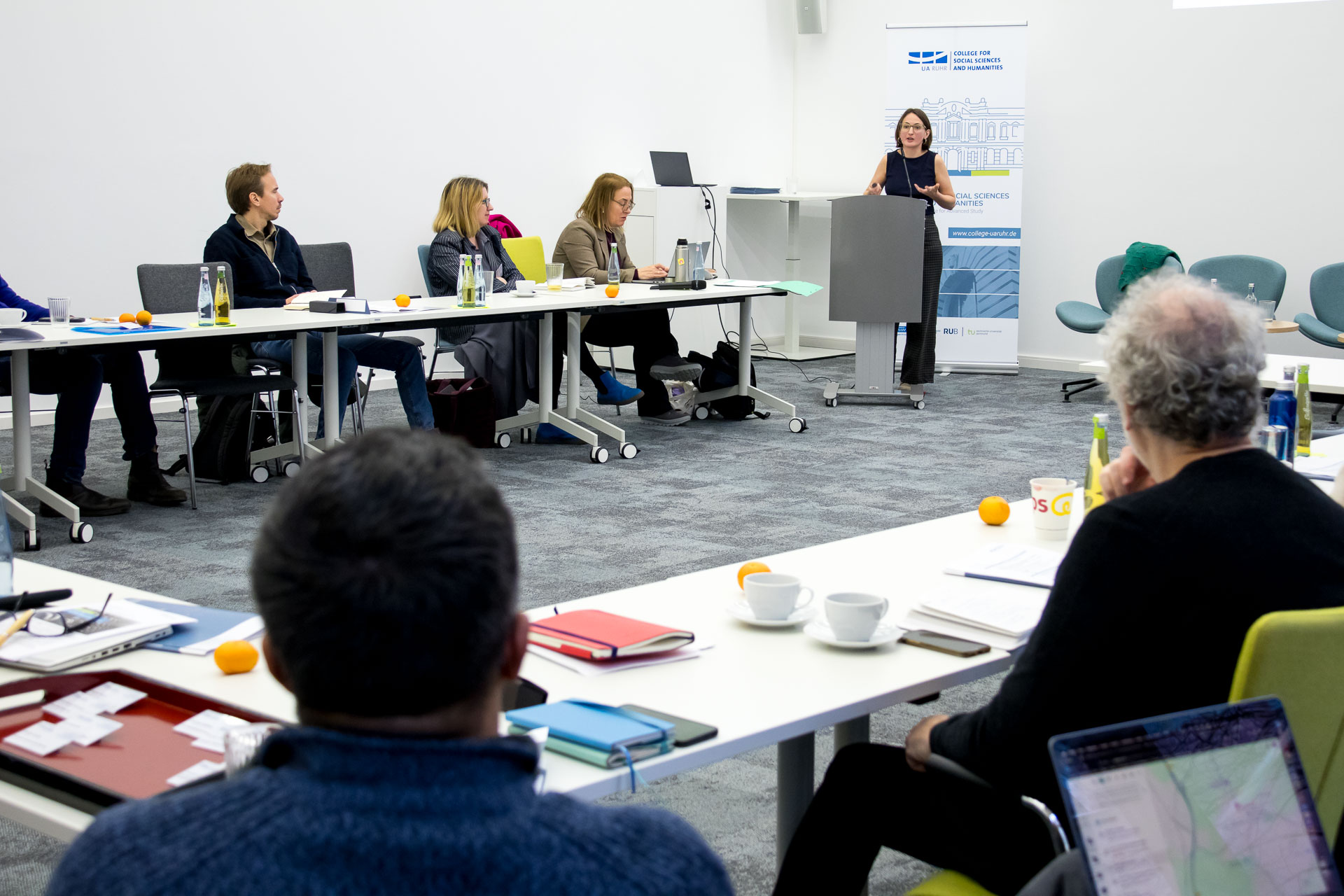 photo from the workshop 'Perpetrator Memory in Spanish culture', participants sitting at a table, a speaker presenting, a screen with slides in the back