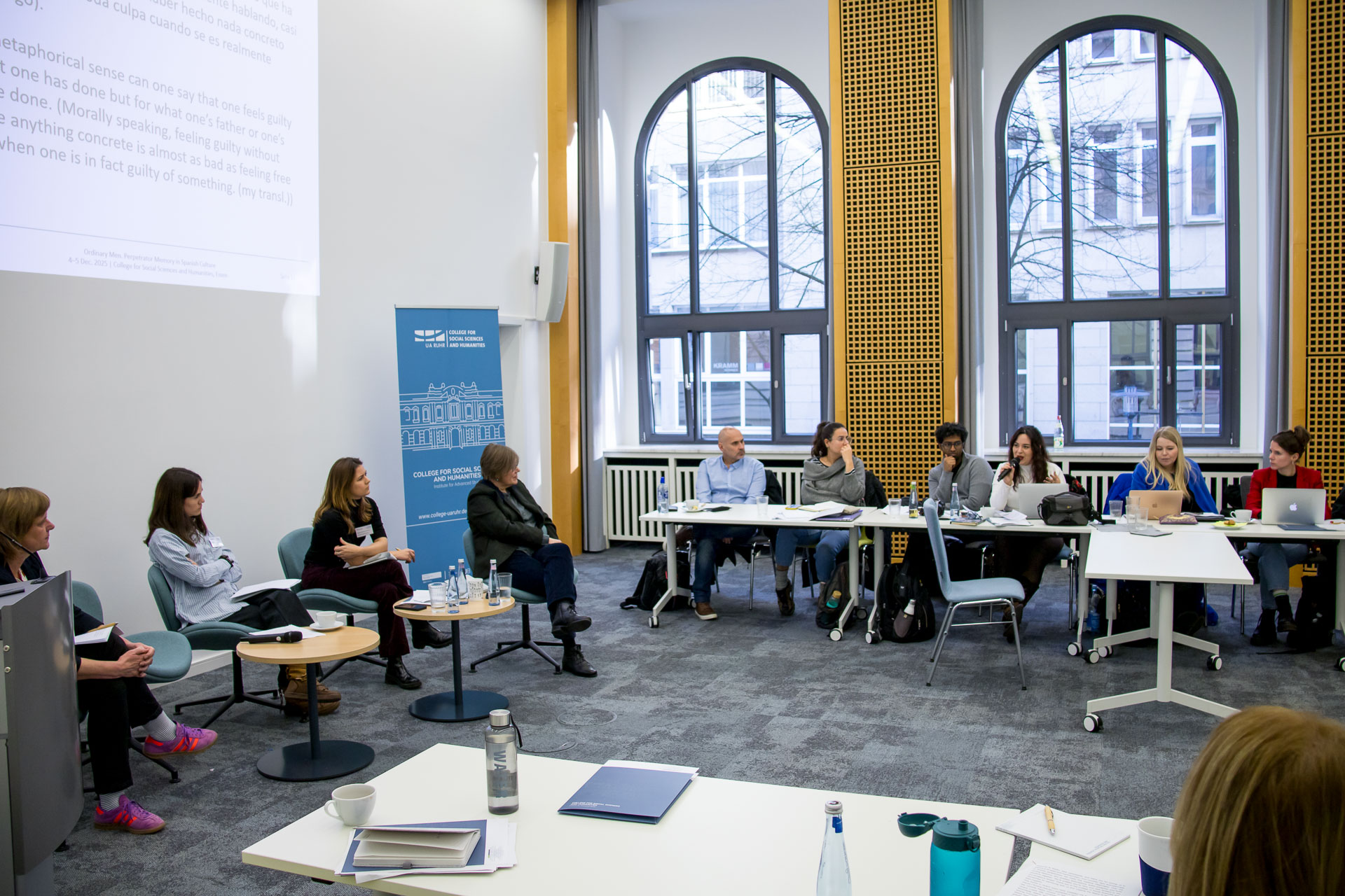 photo from the workshop 'Perpetrator Memory in Spanish culture', panellists sitting around a table, a screen with slides in the back