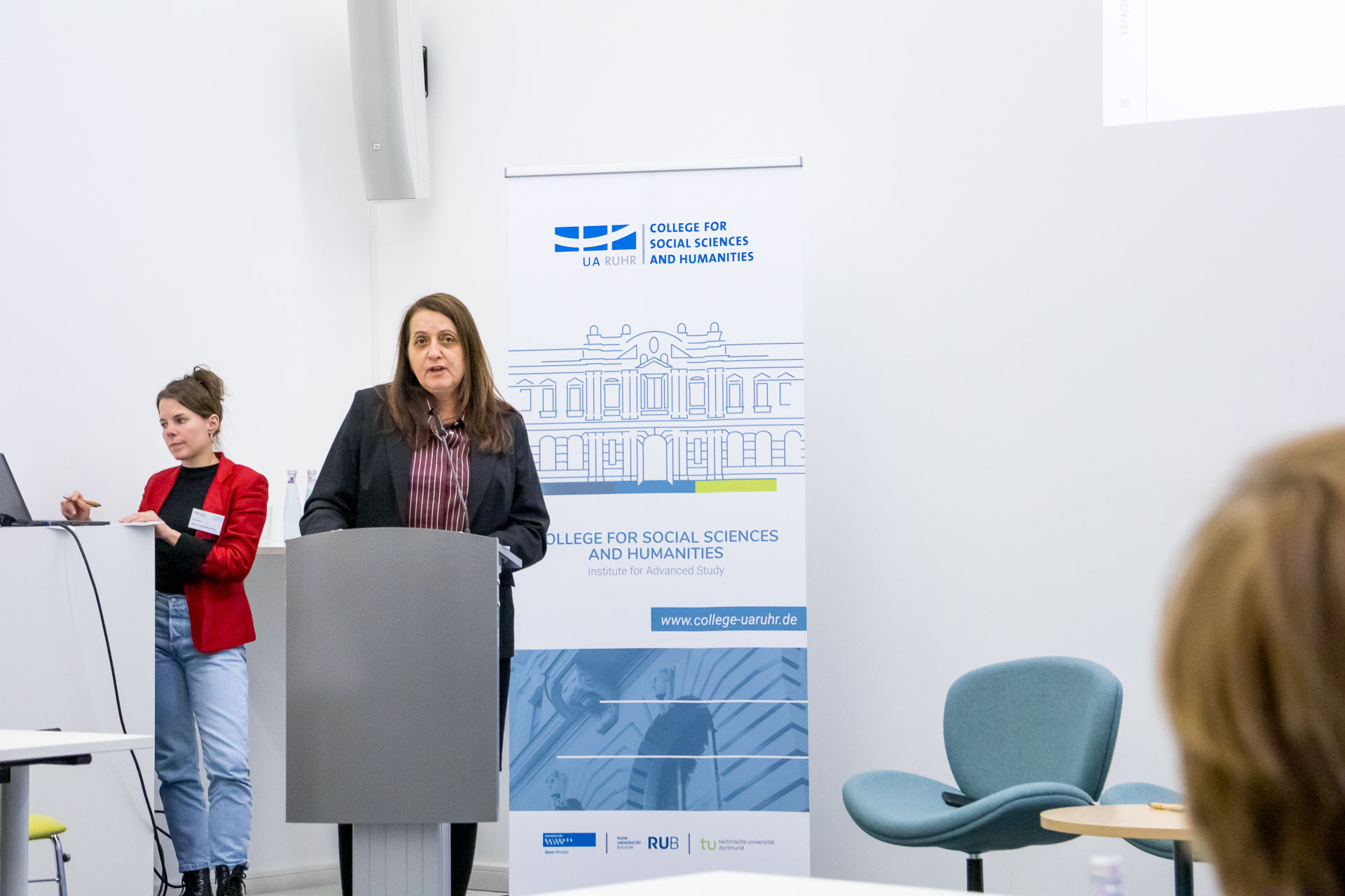 photo from the workshop 'Perpetrator Memory in Spanish culture', participants sitting around a table, a speaker presenting, a screen with slides in the back